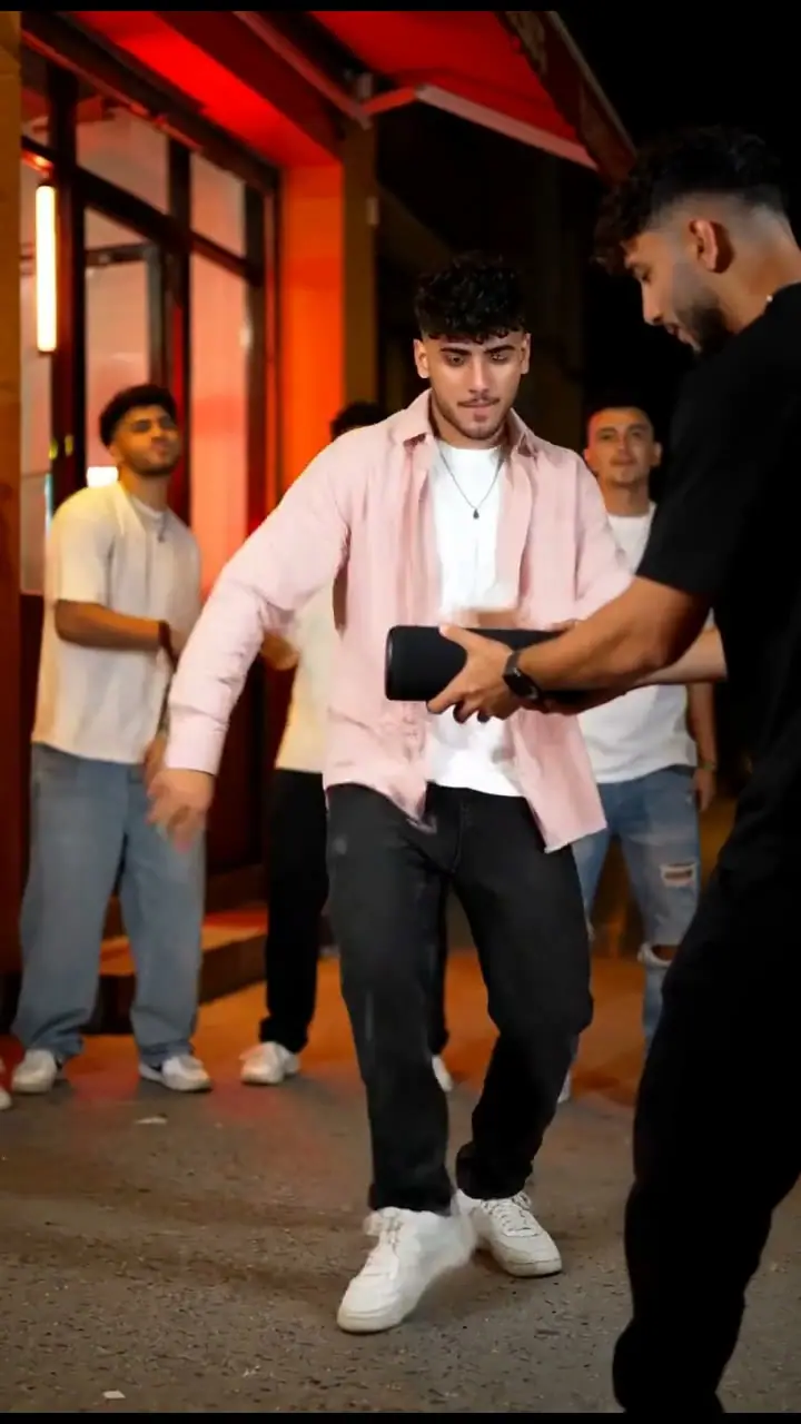 Fictional adult street freestyler in a pink overshirt beside a friend holding a black speaker
